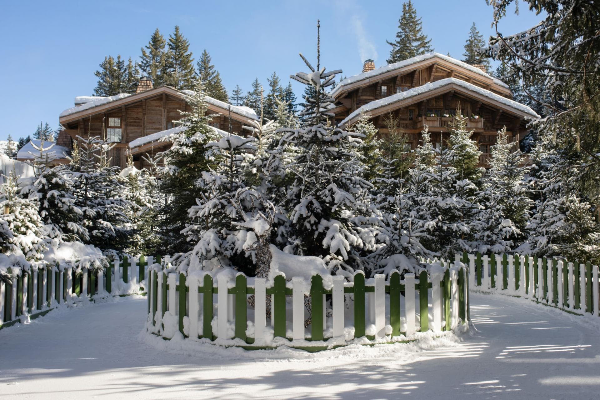 Snow-covered garden area with picket fence and view of chalets