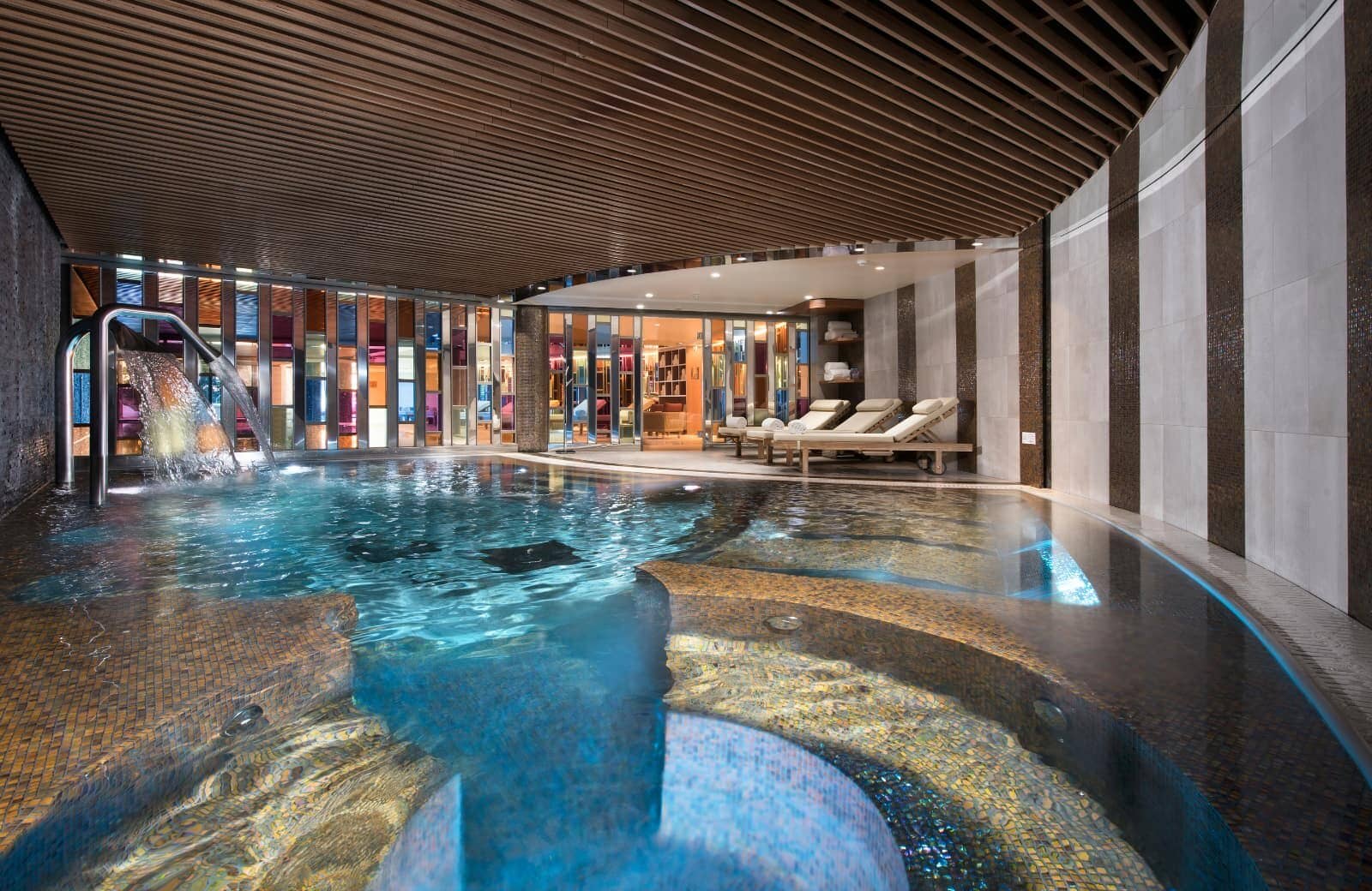 Indoor pool with waterfall feature and poolside lounge seating