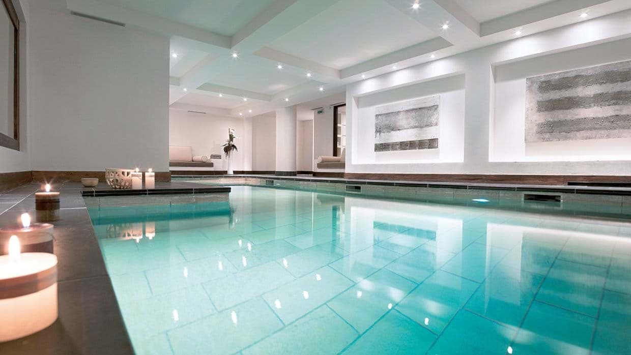 Indoor heated pool with recessed lighting and poolside lounge seating