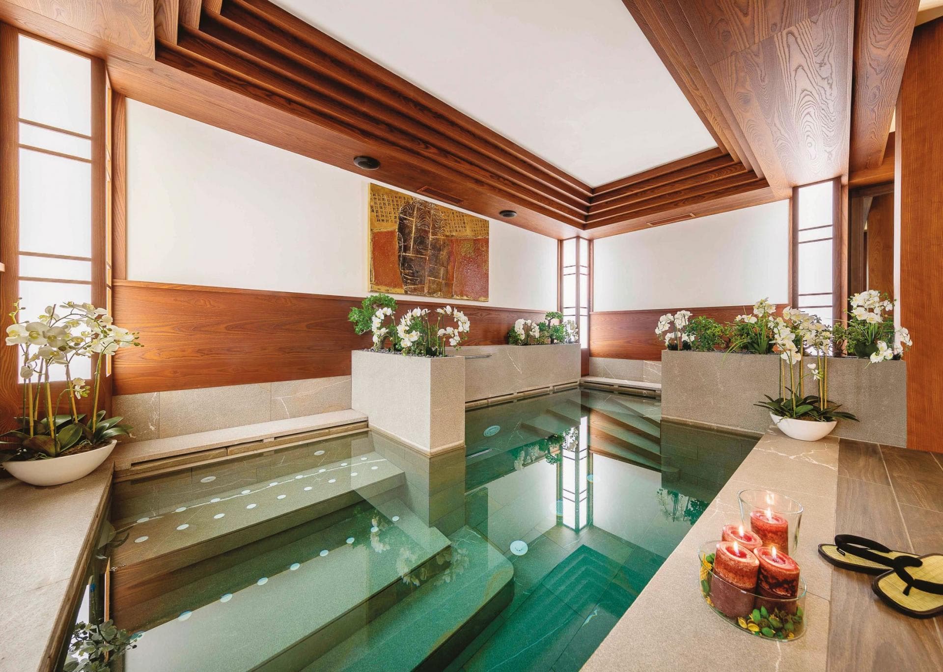 Indoor heated pool with integrated stone steps and wood-paneled ceiling