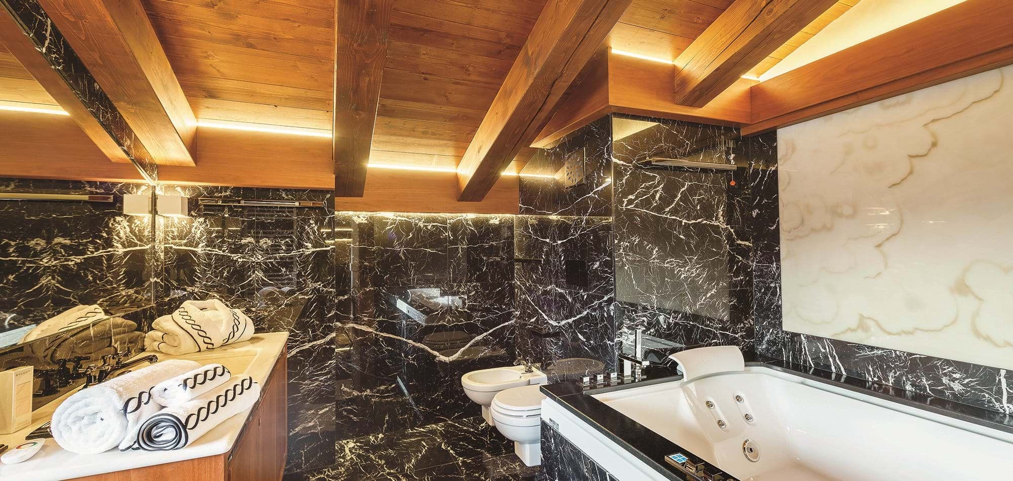 Bathroom with marble walls, jetted soaking tub, and vaulted timber ceilings
