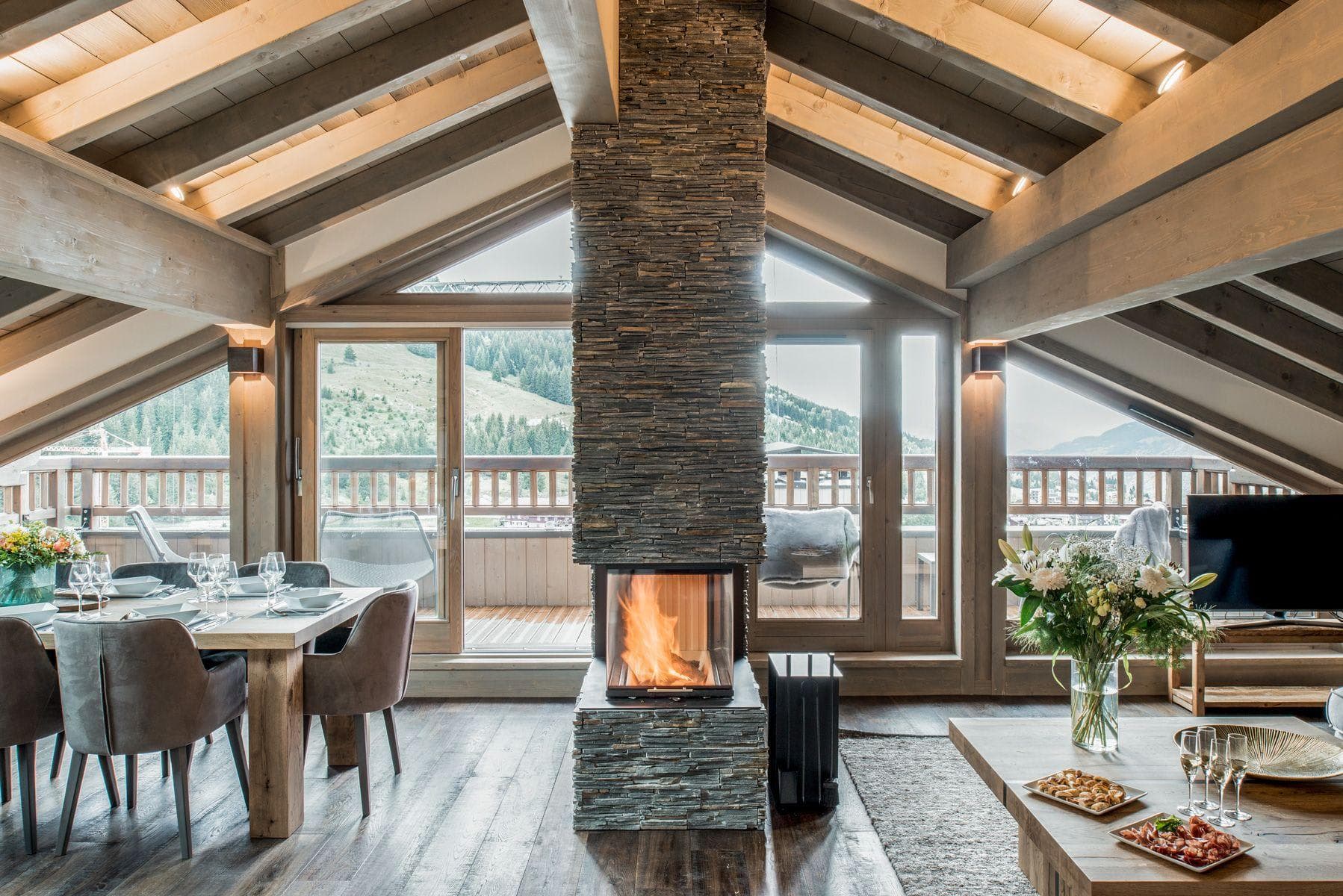 Open-plan living area with three-sided stone fireplace and mountain-view balcony