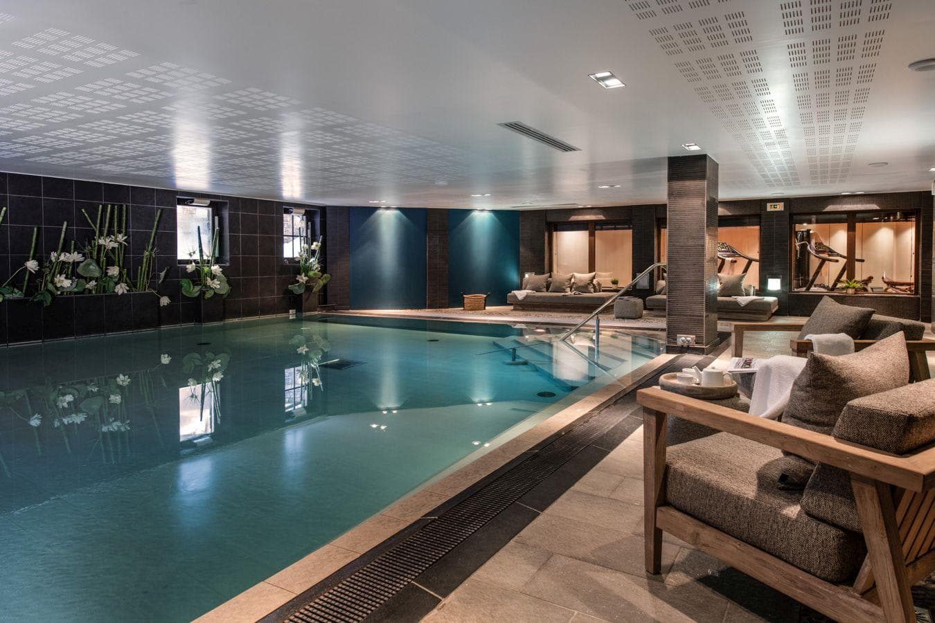 Indoor pool with loungers and adjacent glass-walled fitness room