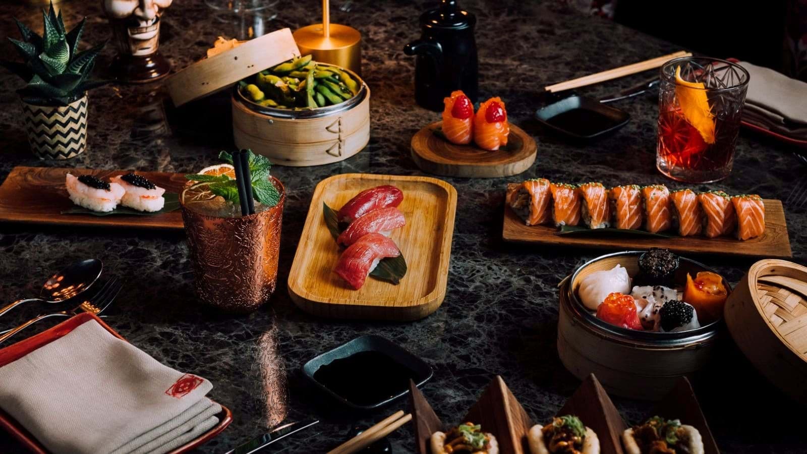 Dining table featuring assorted sushi, dim sum, and craft cocktails
