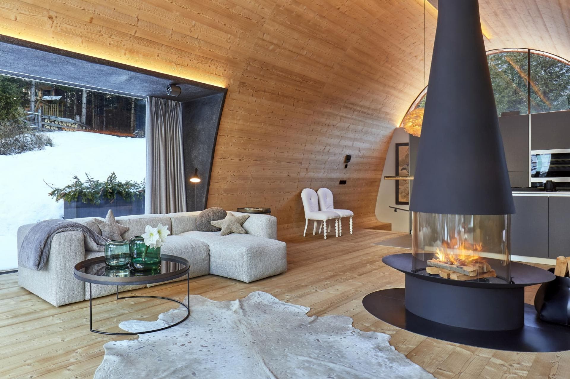 Open-plan living area with suspended 360-degree fireplace and vaulted timber ceilings