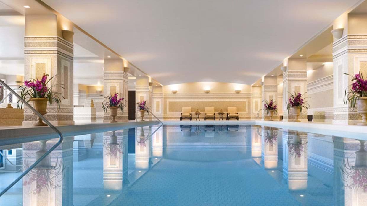 Indoor pool with decorative stone columns and poolside lounge seating