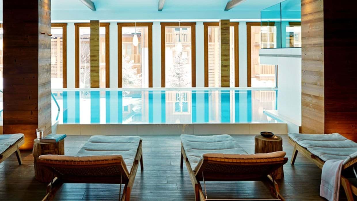 Indoor swimming pool with lounge seating and floor-to-ceiling mountain views