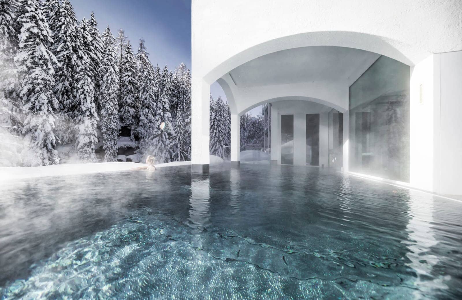 Heated outdoor pool with white arches and snowy forest views
