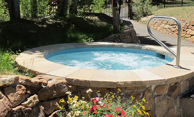 Outdoor hot tub with handrail and surrounding stone masonry