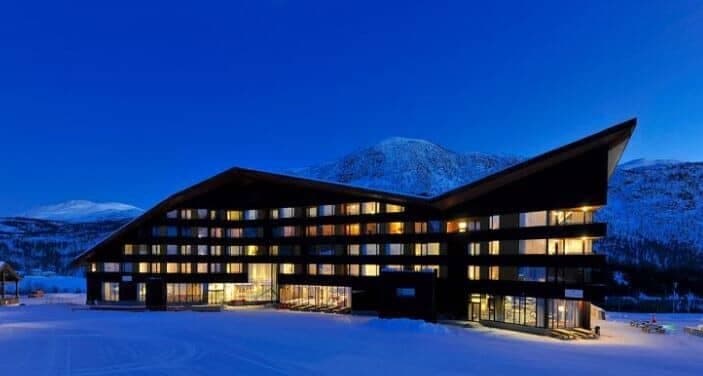 Ski-in, ski-out resort exterior with mountain views and floodlit snowy surroundings