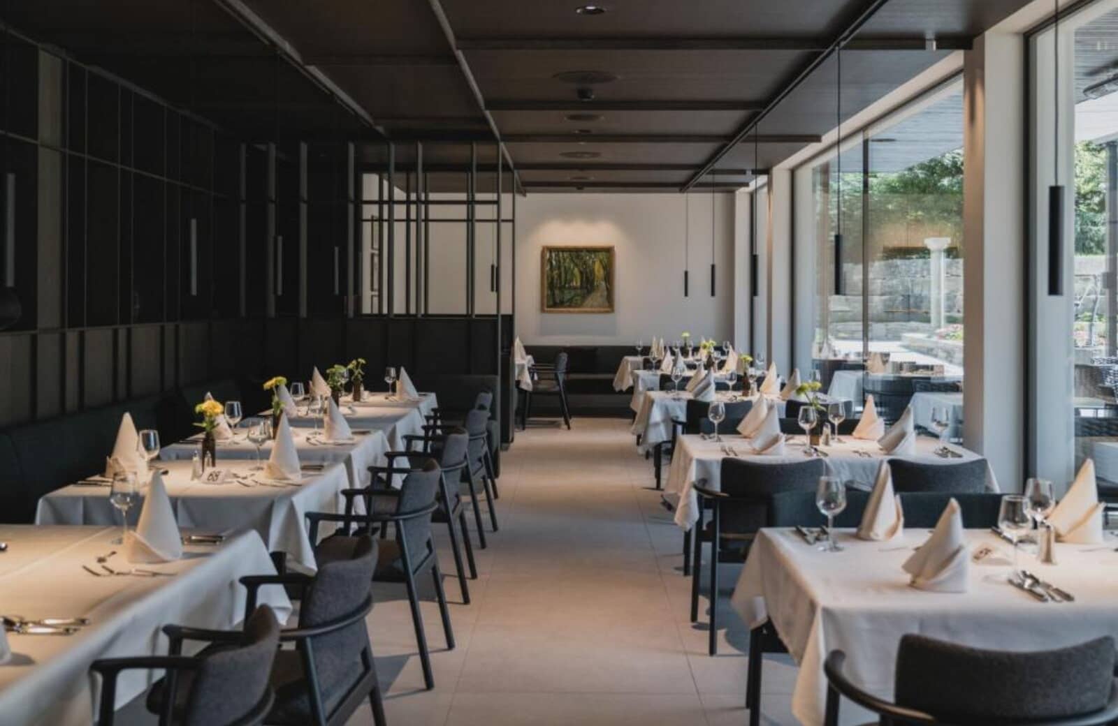 Dining room with white linens, floor-to-ceiling windows, and garden views