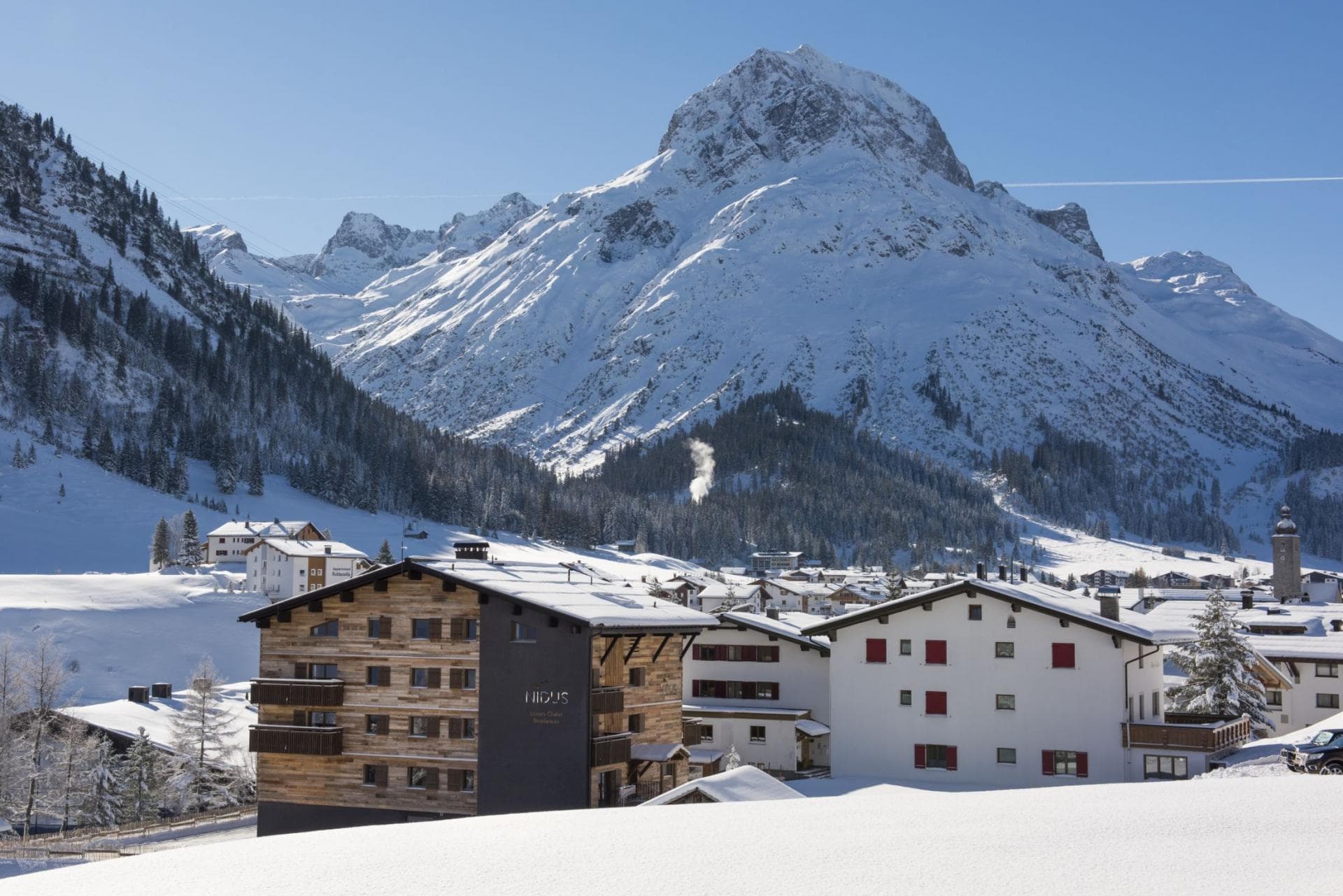 Alpine village with snow-covered peaks; property nestled near lake and ski terrain