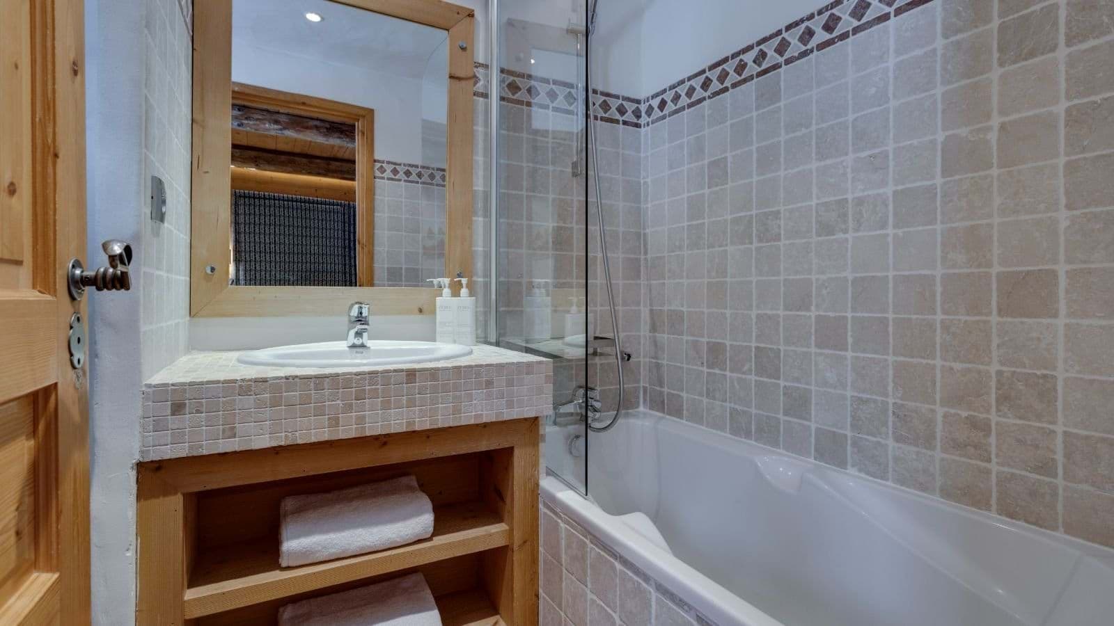Bathroom with stone tilework and bathtub with glass shower screen