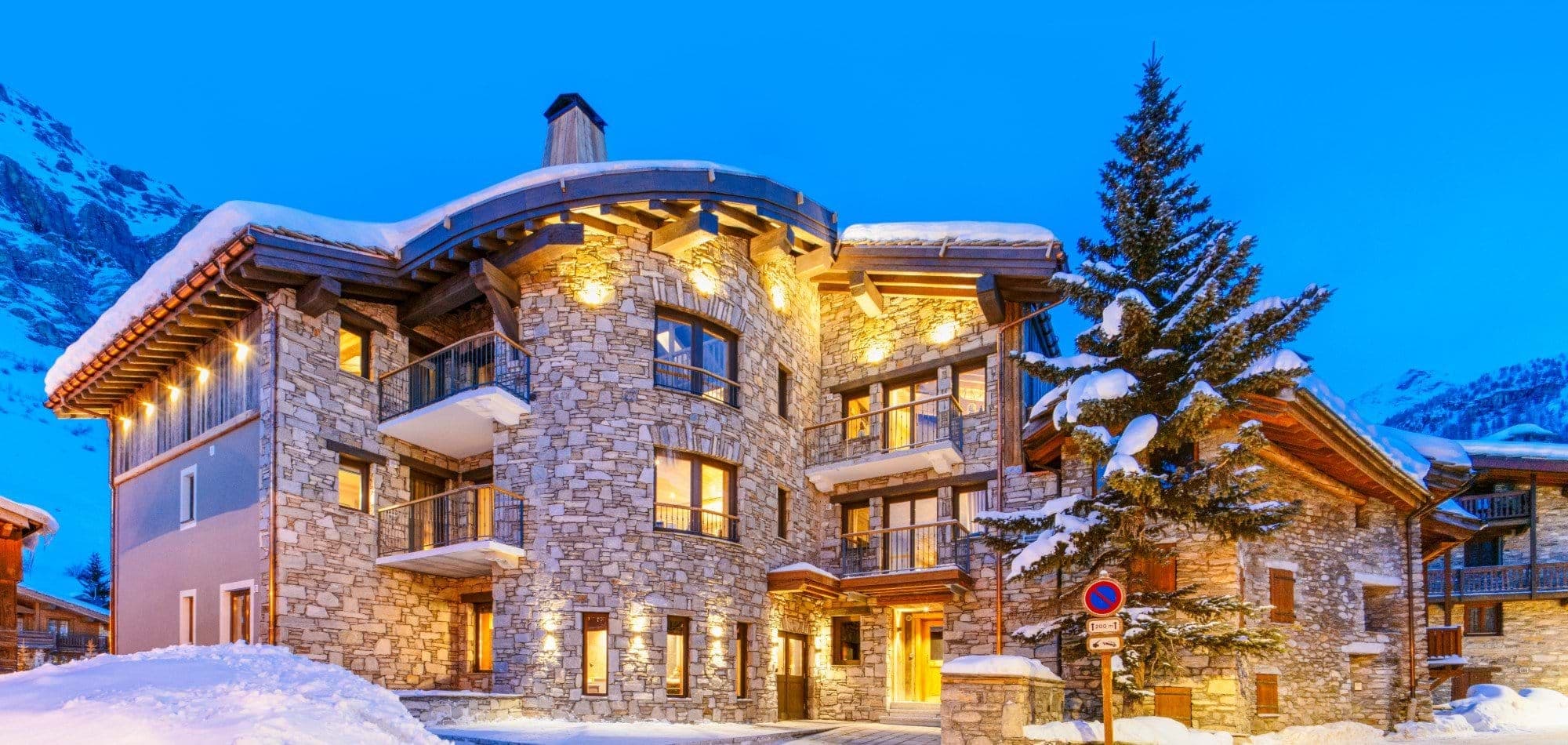 Stone chalet exterior with multiple private balconies and mountain backdrop