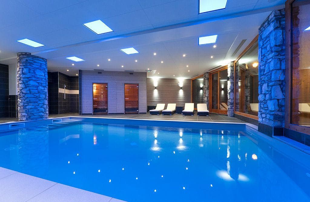 Indoor heated pool with sauna, steam room, and poolside lounge seating