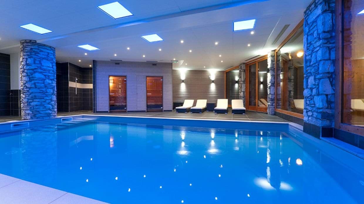 Indoor pool area with dual saunas and poolside lounge seating