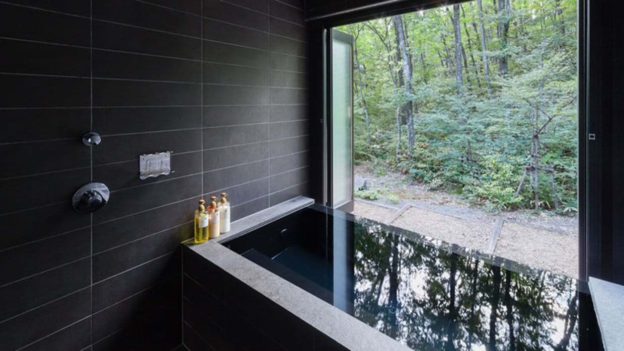 Stone soaking tub with forest views and floor-to-ceiling folding window