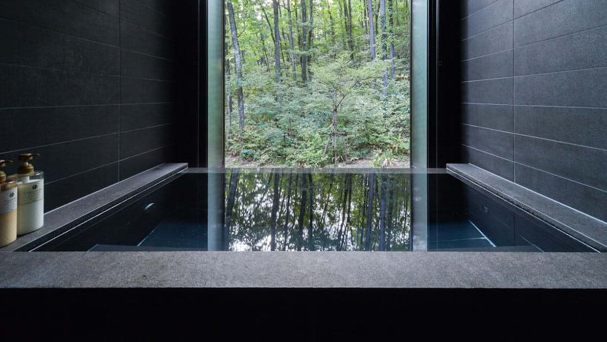 Stone soaking tub with floor-to-ceiling forest views