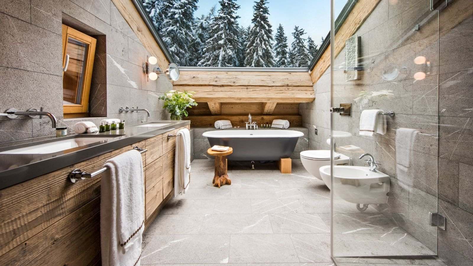 Bathroom with dual vanity, soaking tub, and skylight views of pine forest