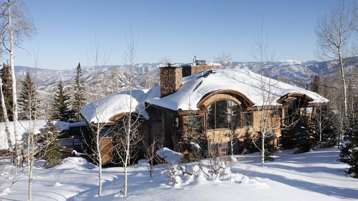 Stone-clad mountain lodge with panoramic valley views and snow-covered grounds