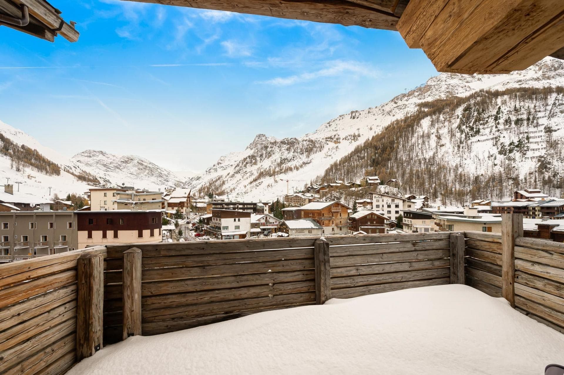 Private balcony with wooden railings overlooking snow-capped village and mountains