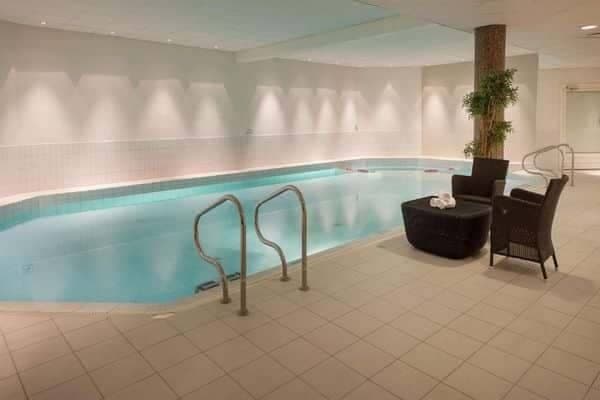 Indoor heated pool with poolside lounge seating and ladder access