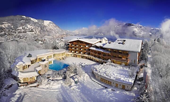 Aerial view of resort featuring heated outdoor pool and lakeside mountain backdrop