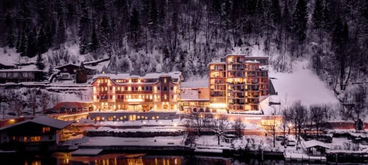 Lakeside mountain resort with illuminated facade and snow-covered forest backdrop