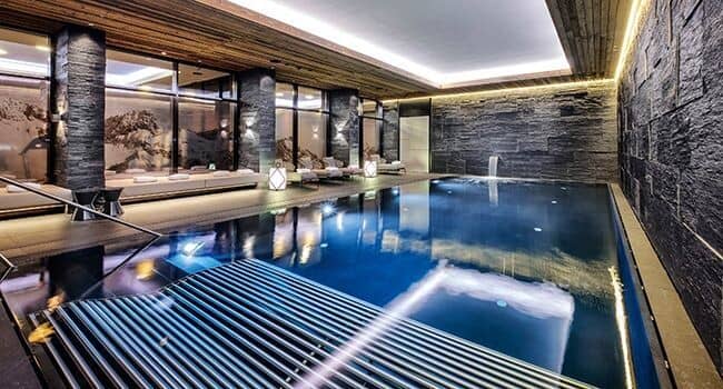 Indoor heated pool with stone walls and poolside lounge seating