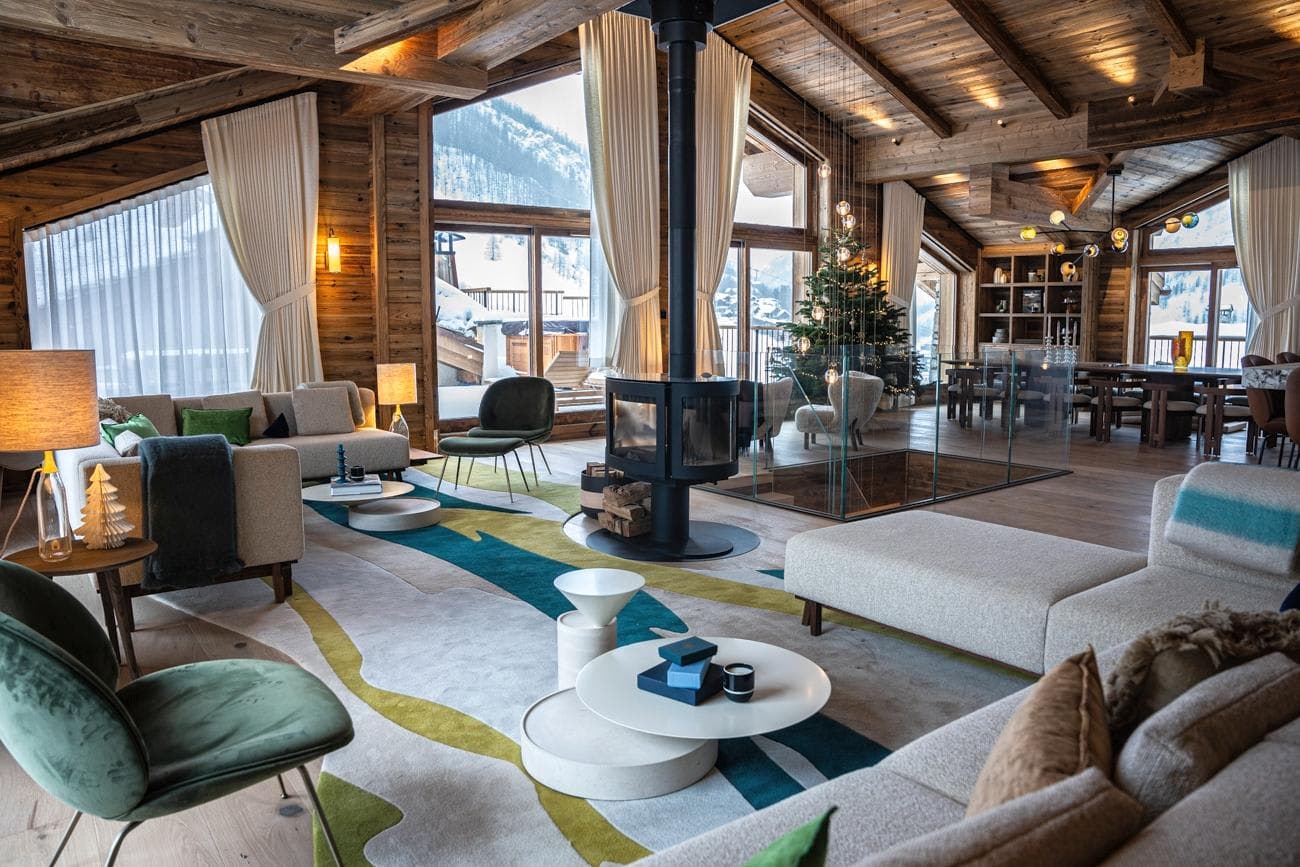 Open-plan living area featuring central 360-degree fireplace and vaulted timber ceilings