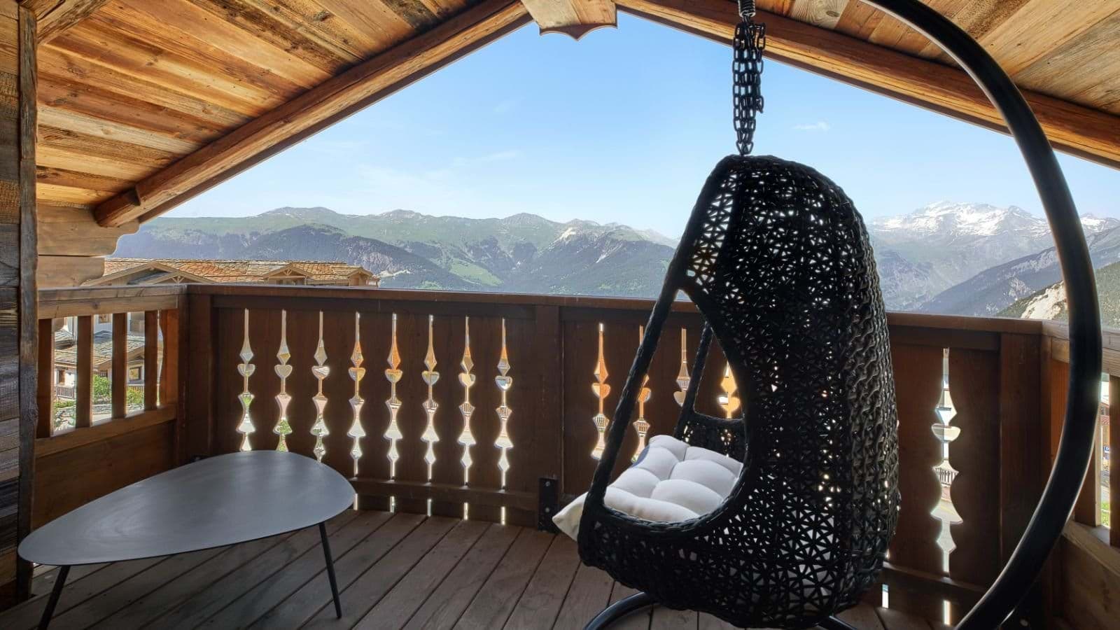 Covered balcony with hanging egg chair and panoramic alpine views