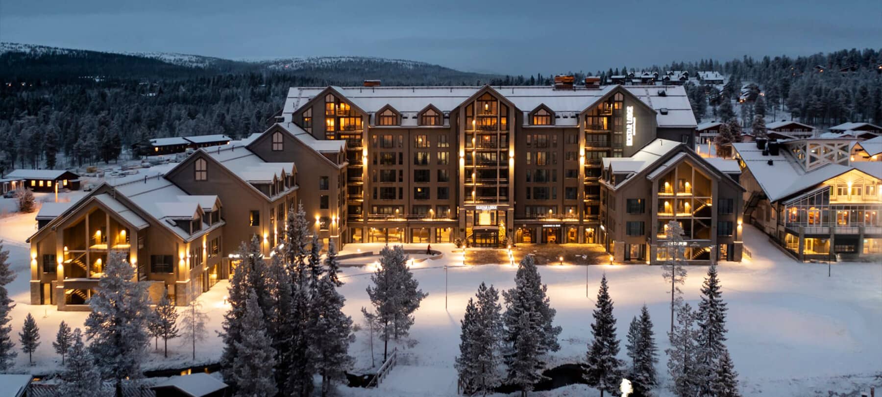 Ski lodge exterior at dusk with snow-covered grounds and mountain views