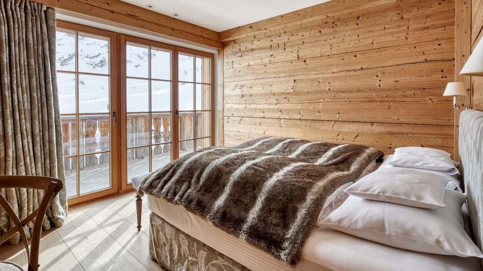 Wood-paneled bedroom with balcony access and snowy mountain views