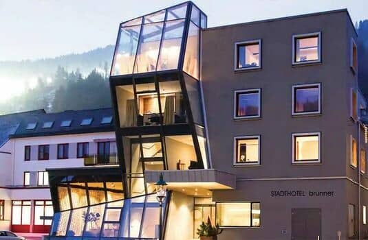 Hotel exterior featuring floor-to-ceiling glass solarium and mountain forest backdrop