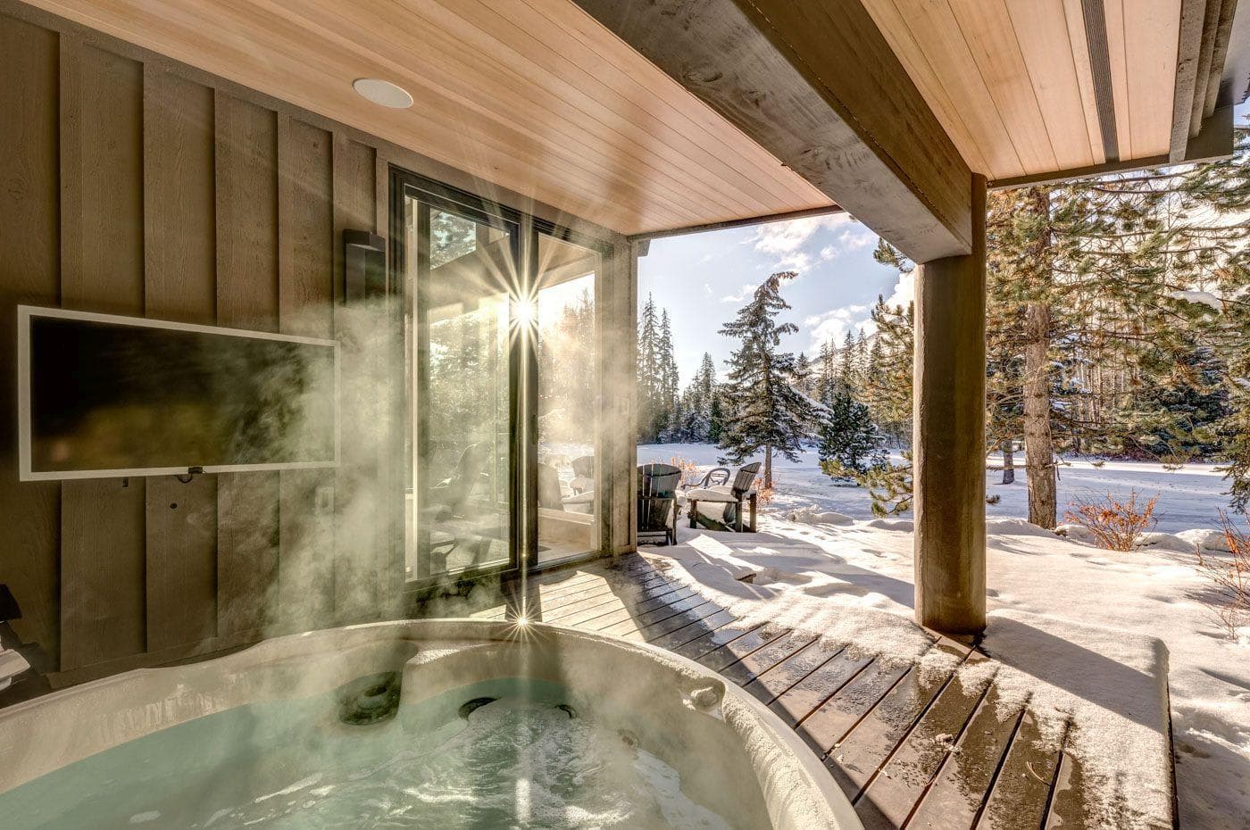 Covered outdoor hot tub with mounted TV and forest view