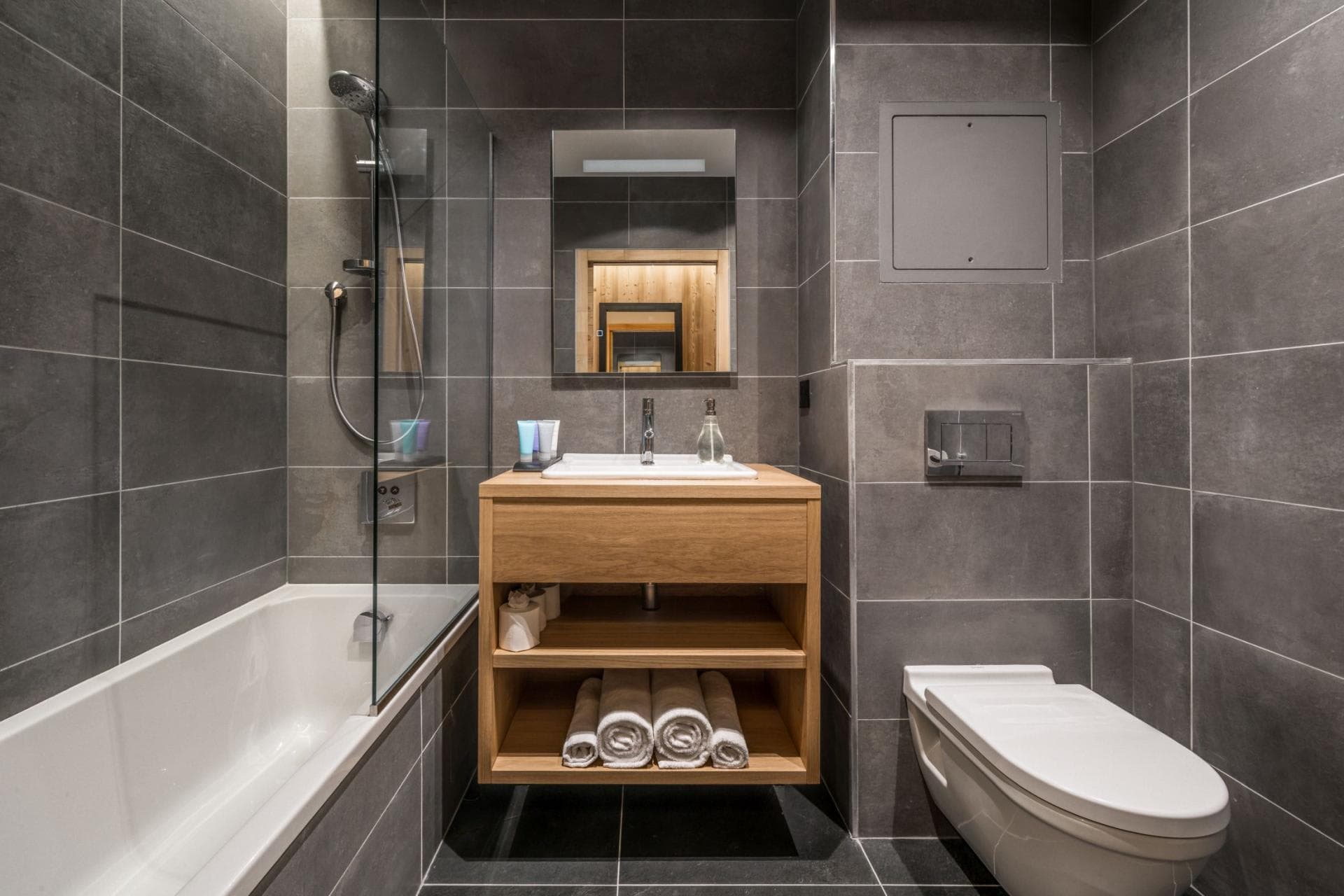 Bathroom with handheld shower over tub and open-shelf wood vanity