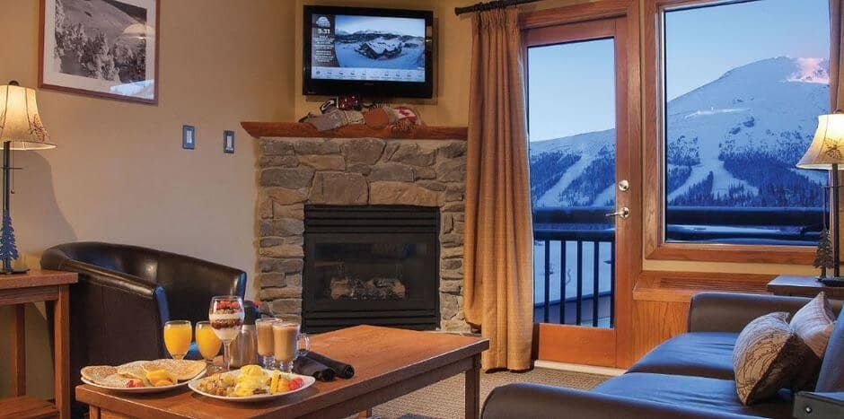 Living area with stone fireplace and private balcony overlooking ski slopes