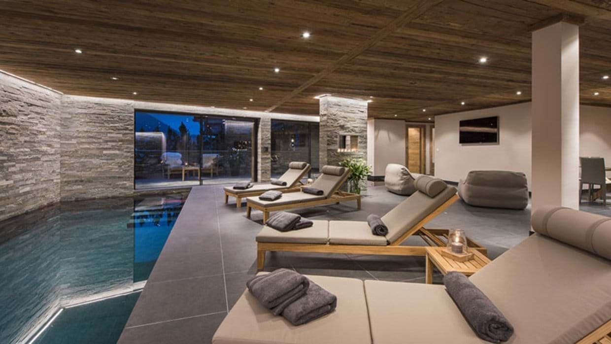 Indoor pool area with loungers, wall-mounted TV, and terrace access