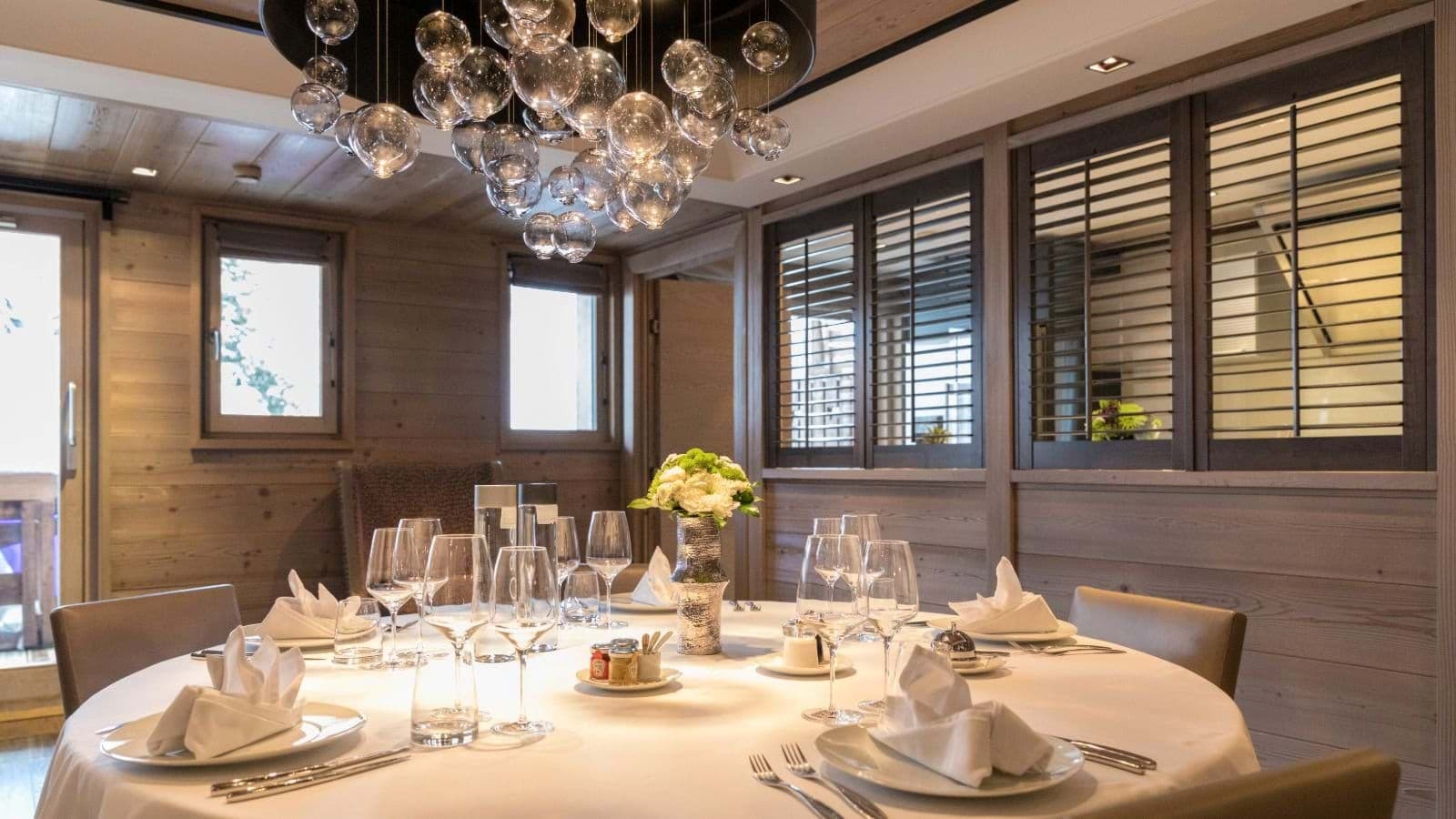 Round dining table seats 8; features glass orb chandelier and wood paneling