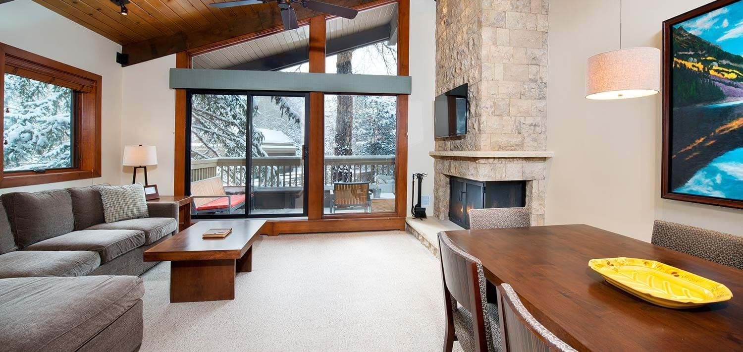 Living area with floor-to-ceiling windows and stone fireplace; access to snowy deck