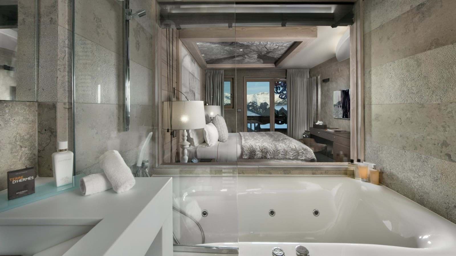 Jetted soaking tub with glass partition to bedroom and mountain views
