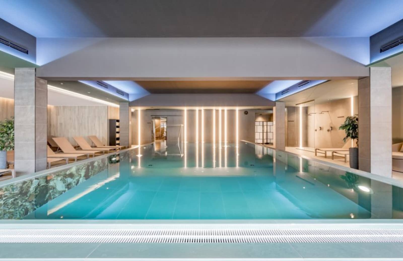 Indoor pool with glass-edge wall and poolside lounge seating