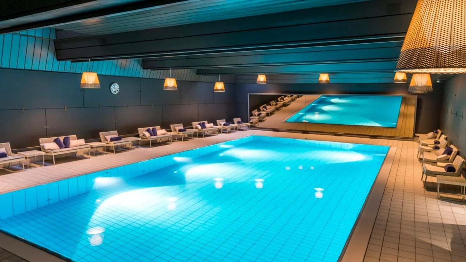 Indoor heated lap pool with poolside loungers and mirrored wall