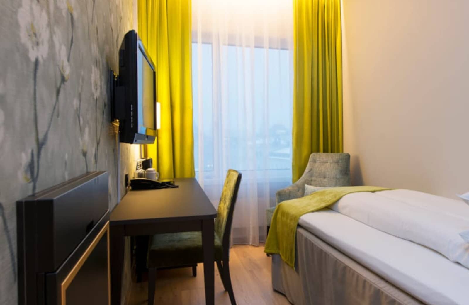 Guest bedroom with single bed and dedicated workspace with wall-mounted TV