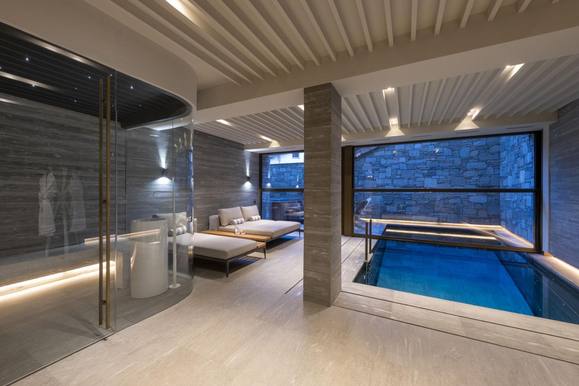 Indoor pool and glass-enclosed steam room with poolside lounge seating