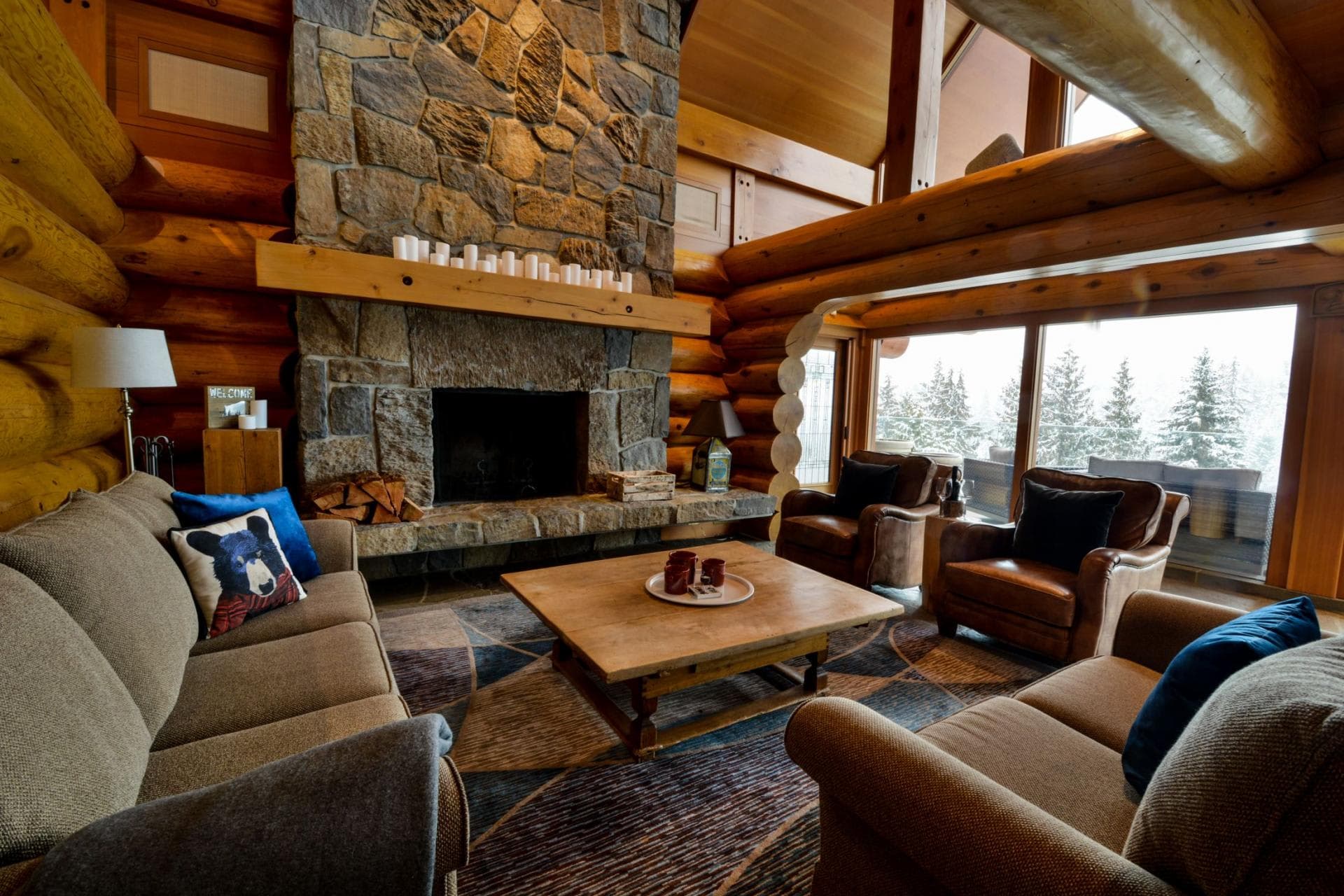 Living room with wood-burning stone fireplace and forest views