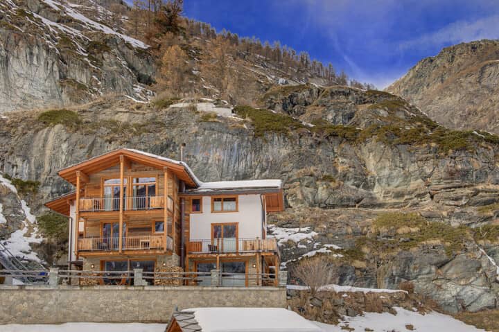 Chalet exterior with multiple balconies and direct mountain cliff backdrop