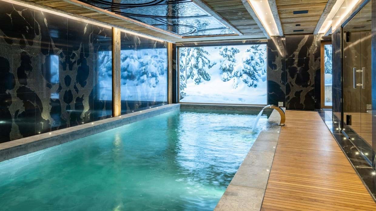 Indoor heated pool with waterfall feature and snowy forest views