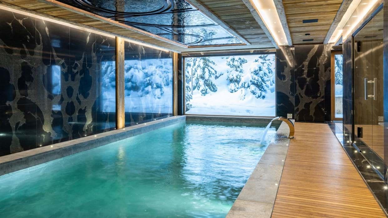 Indoor pool with waterfall feature and views of snow-covered trees