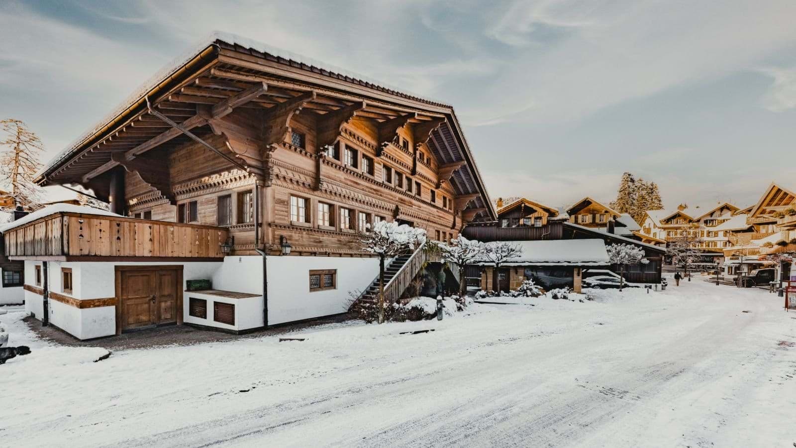 Ski-in chalet exterior featuring garage, upper-level balcony, and snow-cleared access road